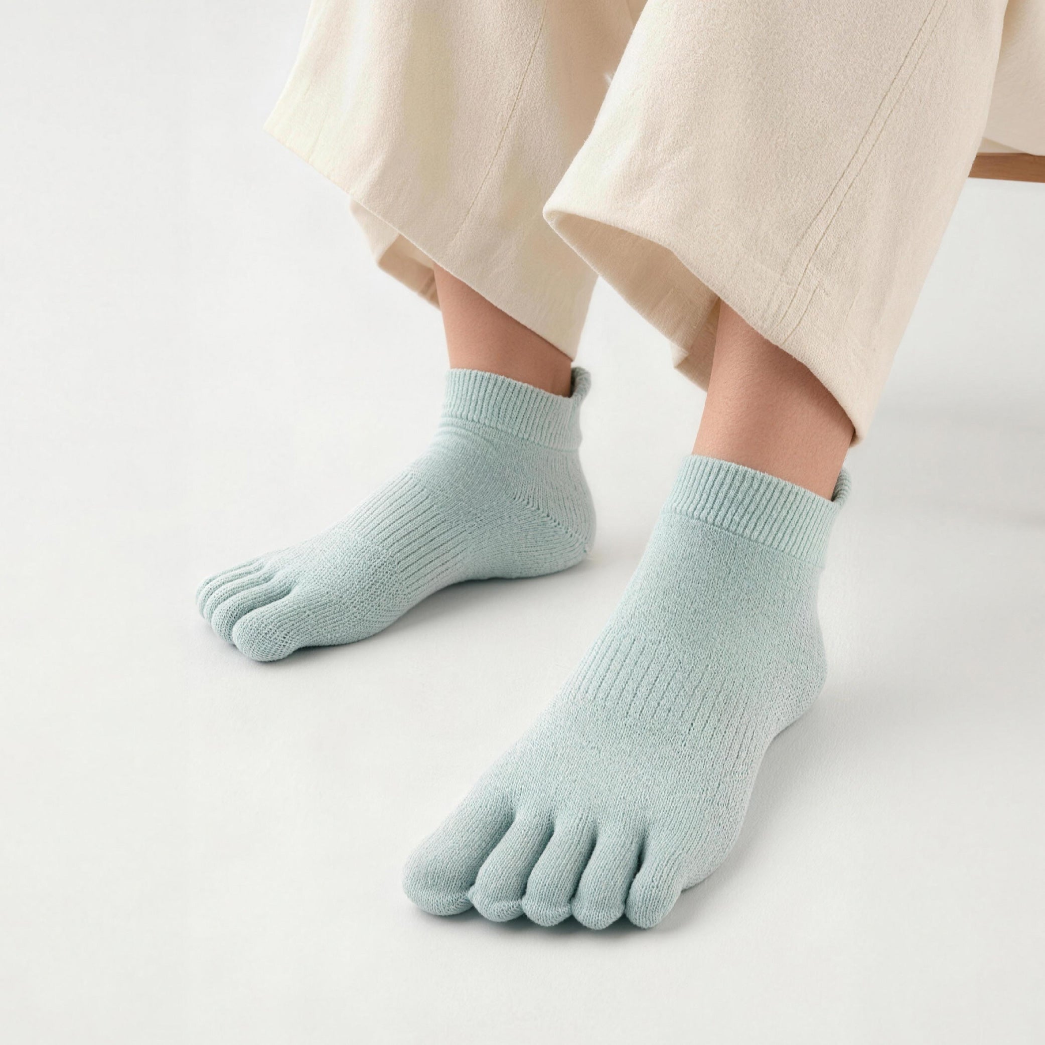 Light blue five-finger socks worn with beige pants on a light background