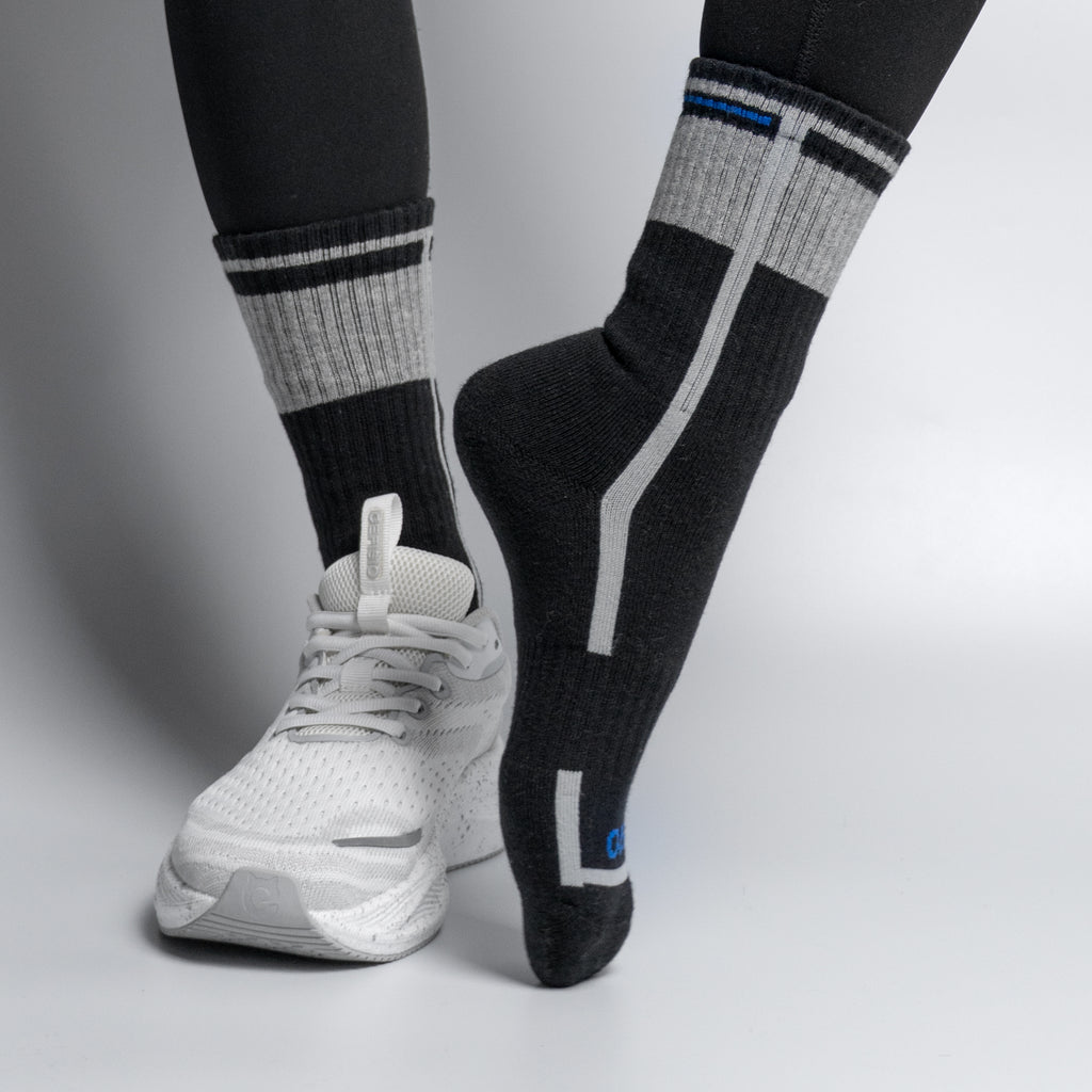 Person wearing black and gray EFISIO All-Day Running socks with white athletic shoes on a light gray background