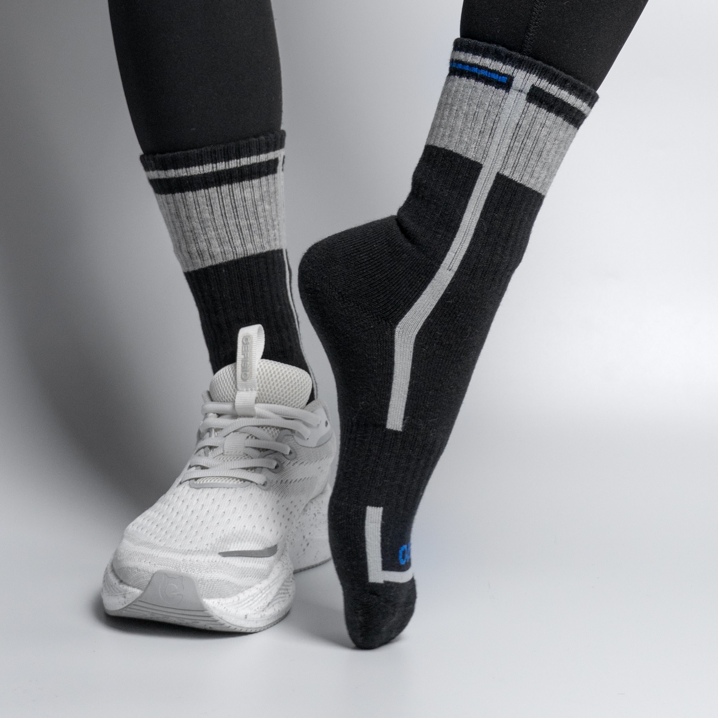 Person wearing black and gray EFISIO All-Day Running socks with white athletic shoes on a light gray background