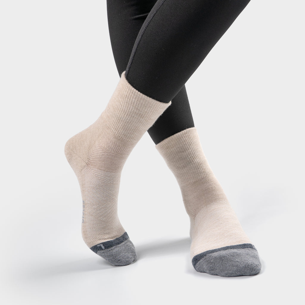 Close-up of a model wearing black leggings and EFISIO Merino Wool Crew Socks with legs crossed, on a white background